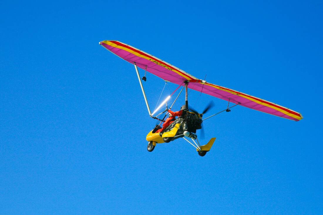 A trike with a pink-and-yellow wing in a clear blue sky