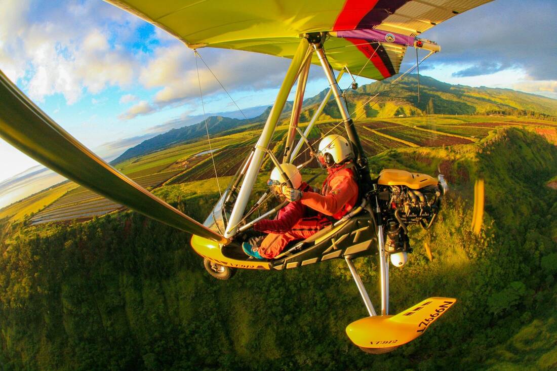 Two aboard the trike above a forested ridge, fields and mountains beyond
