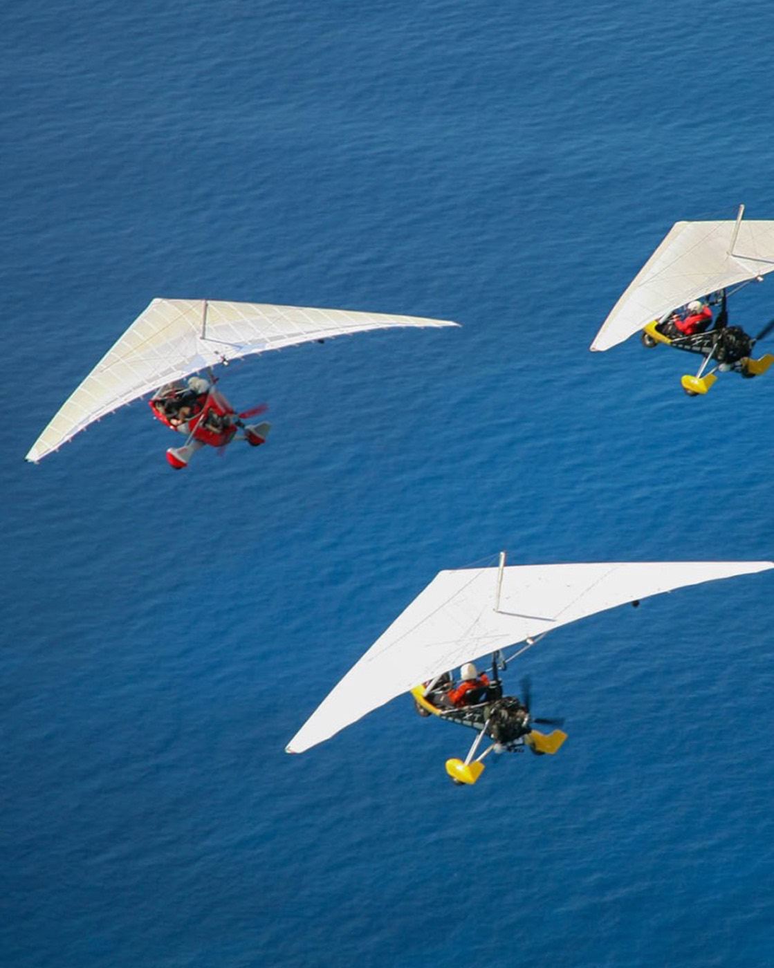 Three trikes with white wings in formation over blue water