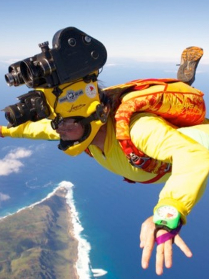 Tom Sanders in freefall wearing a helmet-mounted camera, coastline far below